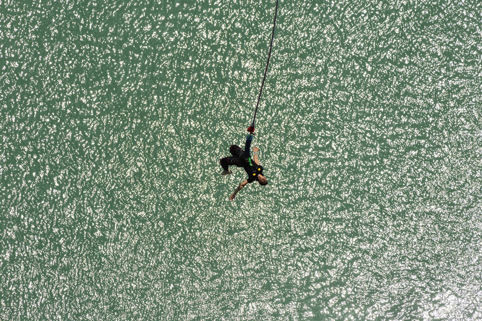 Bungee jumper falling past the emerald-green Ganga river gorge in Rishikesh